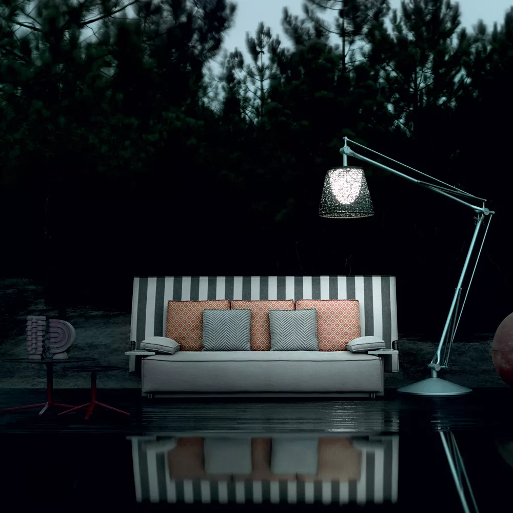 B&B Italia Oh It Rains Sofa steht draußen auf einer Terrasse bei Nacht mit Kissen und einer großen Lampe daneben im Hintergrund sind Bäume.