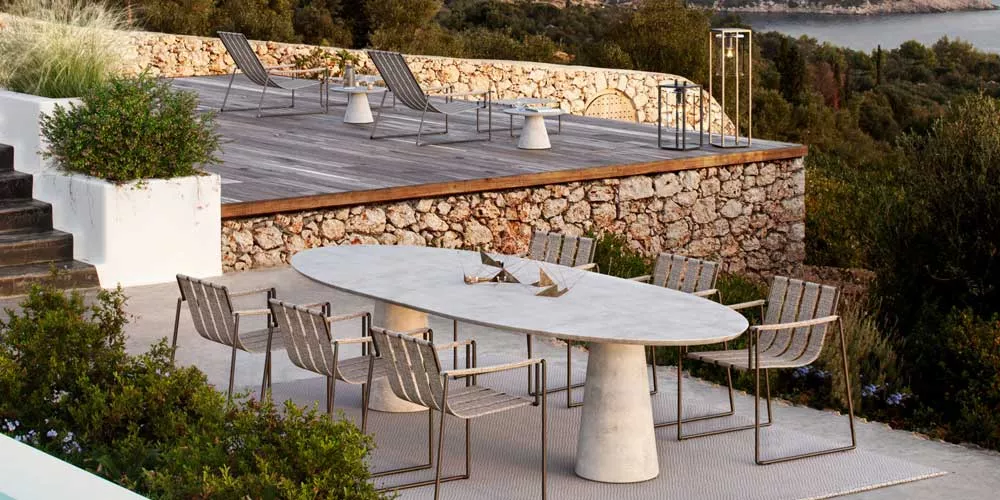 Royal Botania Strappy Essgruppe in Grau auf einer Terrasse mit Steinmauer und Meerblick, stimmungsvolles Outdoor-Setting.