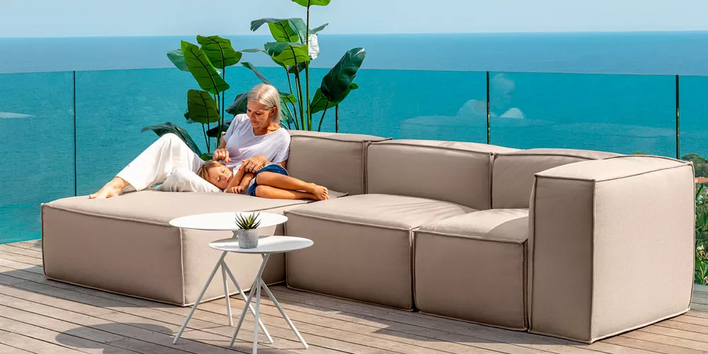 Talenti Ocean Loungegruppe in Beige auf einer Terrasse mit Meerblick, entspannte Atmosphäre, moderne Gartenmöbel-Kollektion.