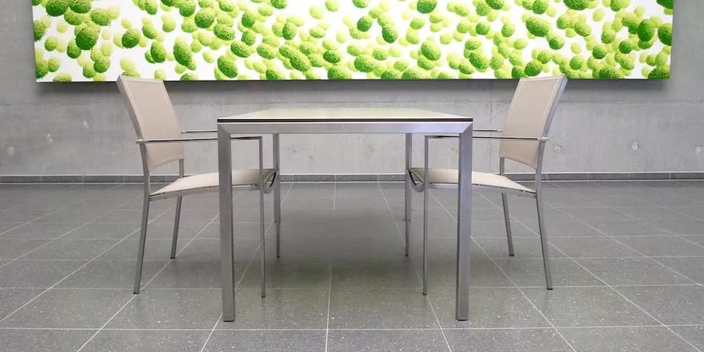 Zwei beige Stühle und ein Tisch von Royal Mirage Vegas auf grauem Fliesenboden vor einer grünen Kunstwand in modernem Ambiente.