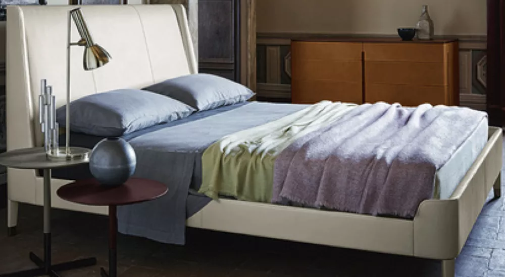 Poltrona Frau Fidelio Notte Bett in Cremeweiß, abgebildet in einem stilvollen Schlafzimmer mit Holzmöbeln und sanfter Beleuchtung.