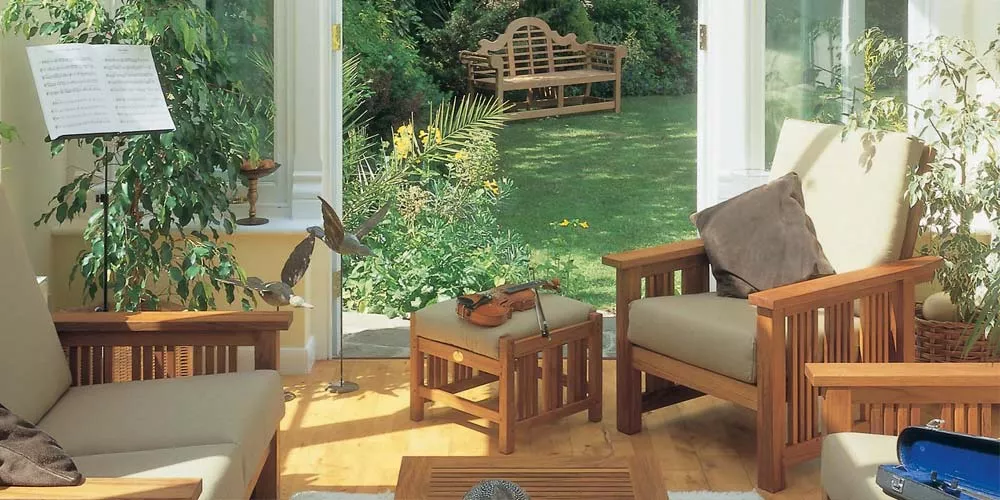 Barlow Tyrie Mission Lounge in Naturholz mit cremefarbenen Polstern in einem sonnigen Wintergarten mit Blick auf den Garten.