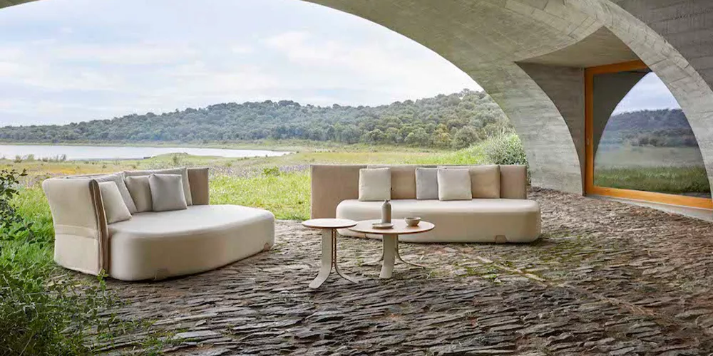 Gandia Blasco Isla Kollektion in Beige auf einer Steinterrasse mit Blick auf eine grüne Landschaft und einen See im Hintergrund.
