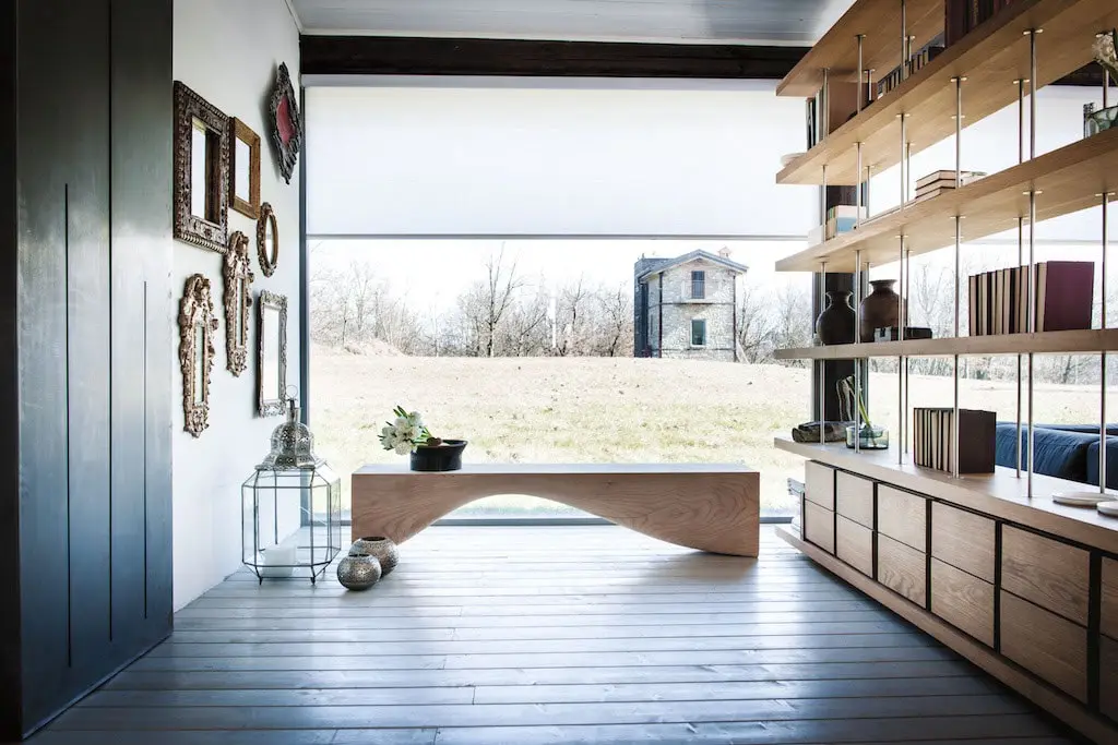 RIVA 1920 Curve Bank aus massivem Zedernholz, naturfarben, auf hellem Holzboden mit schwarzer Vase und weißen Blumen.