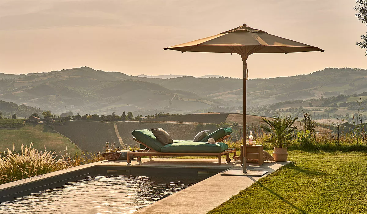 Weishäupl Mittelstockschirm in Beige neben einem Pool mit Blick auf eine hügelige Landschaft bei Sonnenuntergang.