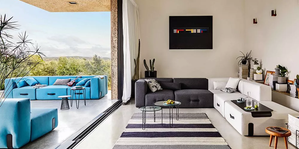 Wohnzimmer mit Conmoto Kollektion Miami in Blau und Weiß, moderne Sofas und Couchtische, Blick auf Terrasse mit Landschaft im Hintergrund.