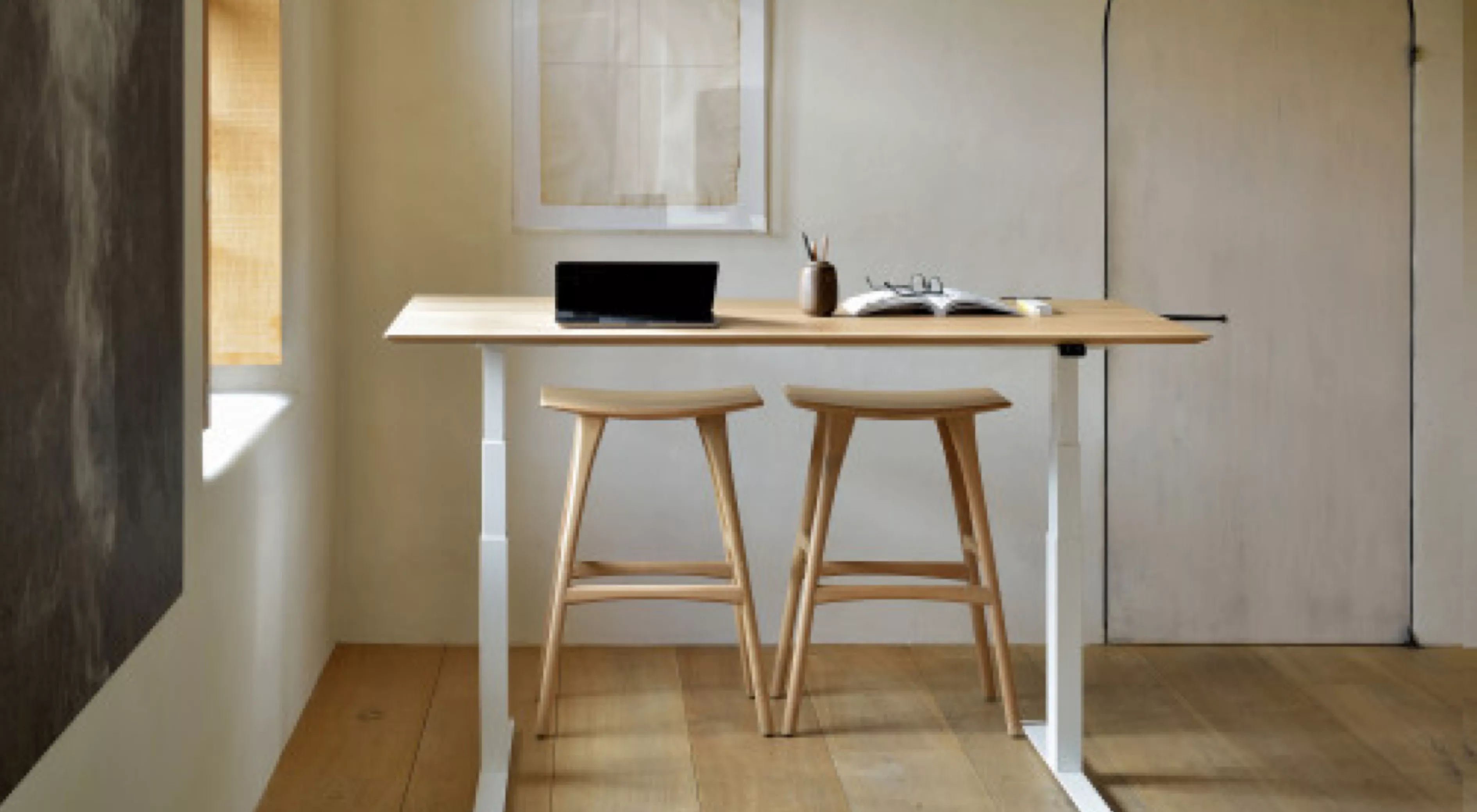 Zwei Holzstühle und ein höhenverstellbarer Tisch in hellem Holzton in einem minimalistischen Raum mit Laptop und Notizbuch auf dem Tisch.