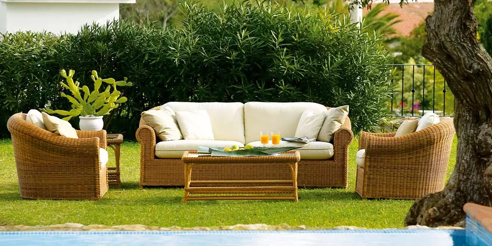 Braune Point Brumas Outdoor-Loungegruppe auf grünem Rasen mit weißem Sofa und Sesseln, Tisch mit Getränken, im Gartenhintergrund.