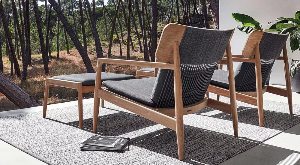 Gartenmöbel-Loungegruppe von Gloster Archi in Holz und Grau auf einer Terrasse mit Waldblick, abgebildet in einer stimmungsvollen Szene.