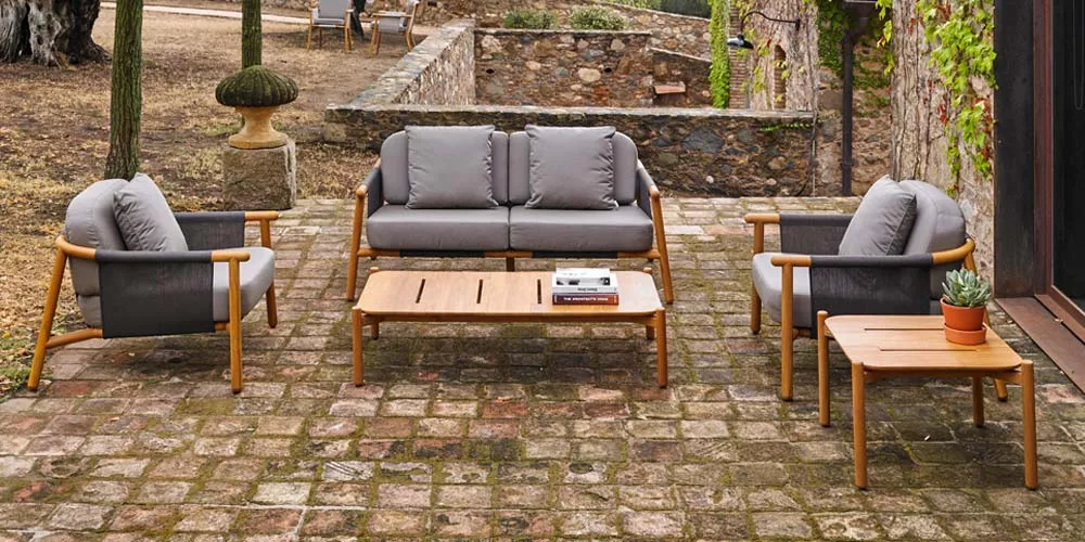 Grau-braune Point Hamp Outdoor Lounge auf rustikalem Steinboden im Garten, bestehend aus Sofa, zwei Sesseln und zwei Tischen.
