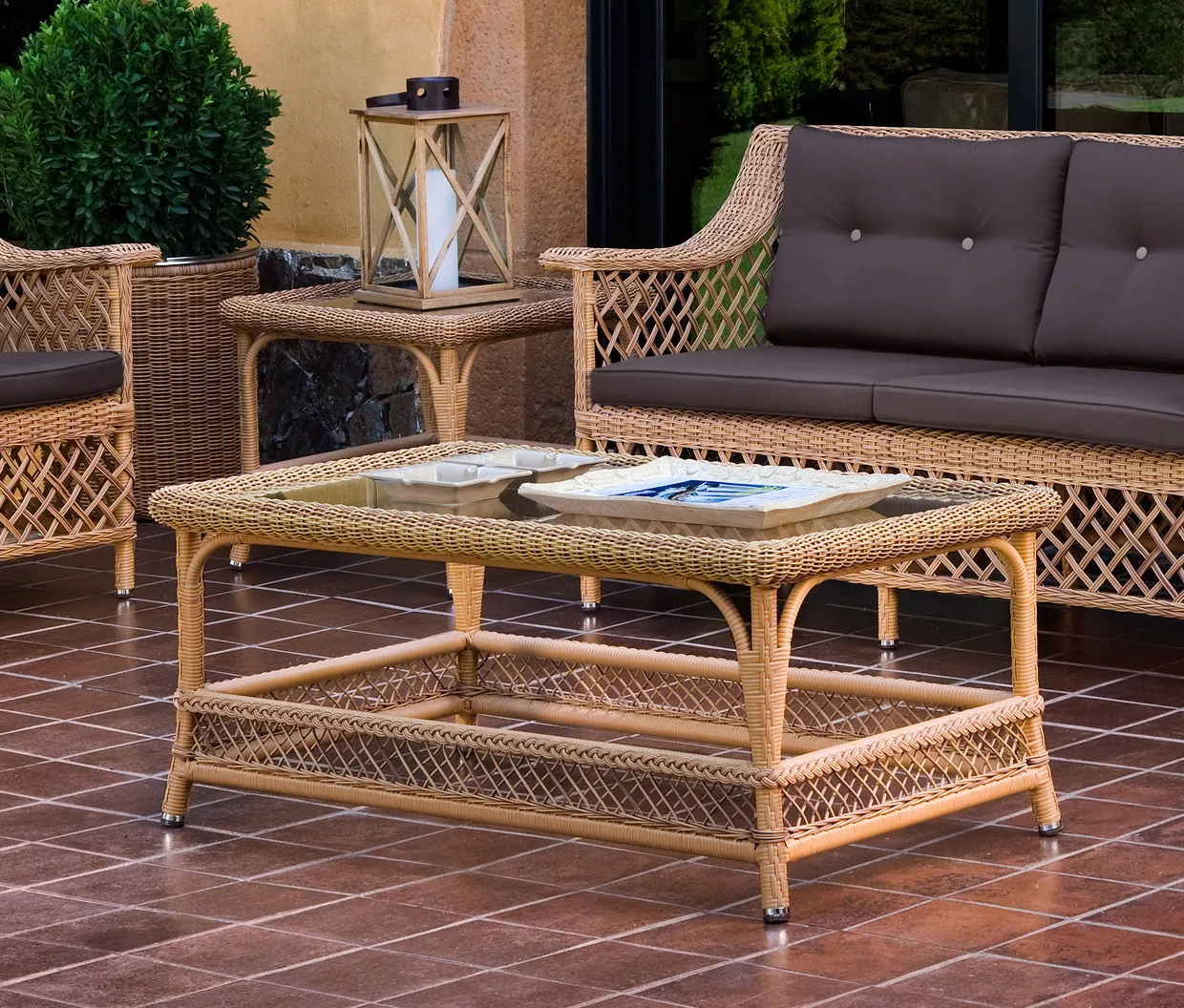 Beistelltisch Arena von Point in Naturfarbe auf einer Terrasse mit Rattanmöbeln und Laterne, umgeben von grünen Pflanzen.