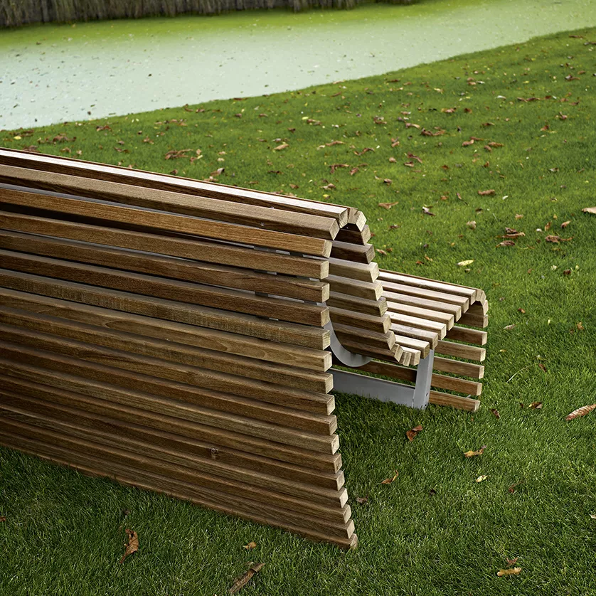 B&B Italia Titikaka Gartenbank aus Holz steht auf einer grünen Wiese neben einem Teich