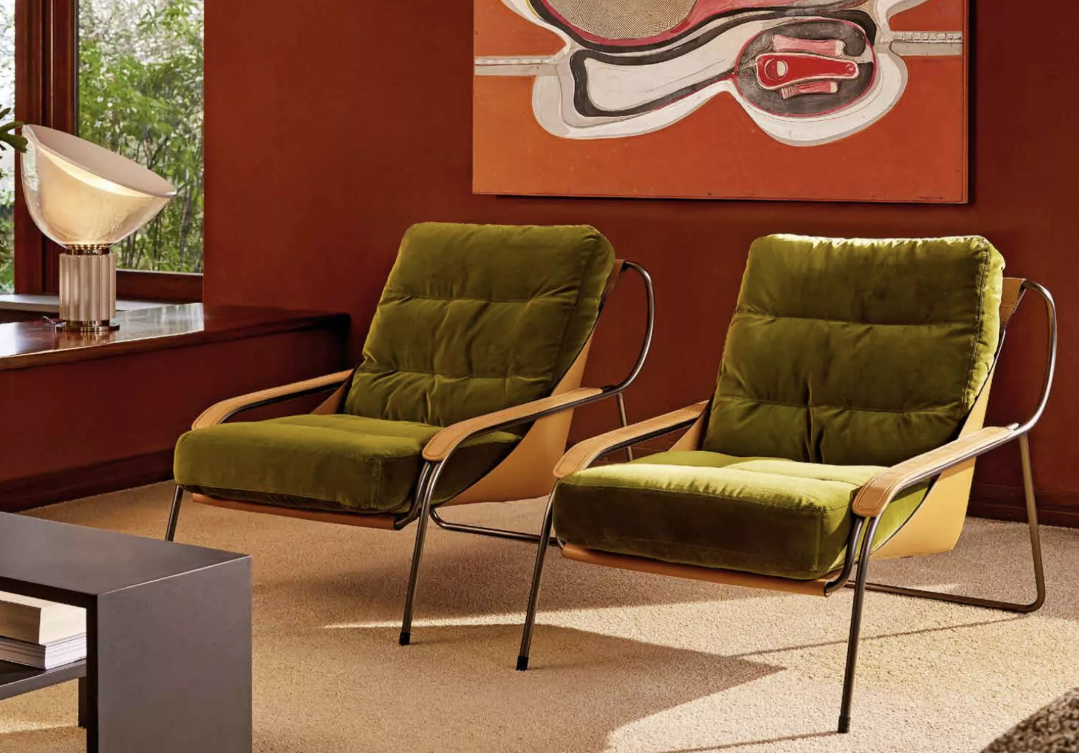 Zwei grüne Zanotta Sessel in einem gemütlichen Wohnzimmer mit roter Wand und Kunstwerk im Hintergrund.
