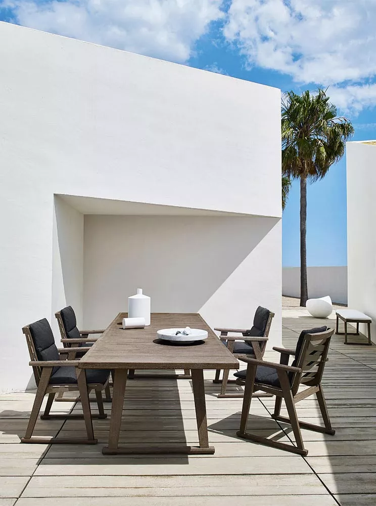 B&B Italia Gio Armlehnstuhl in einem modernen Außenbereich mit Holztisch und Dekoration unter blauem Himmel und Palmen im Hintergrund