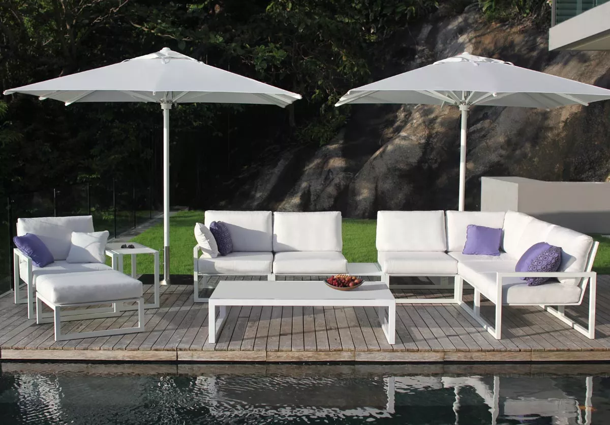 Royal Botania Ninix Lounge Kollektion in Weiß auf Holzterrasse mit zwei Sonnenschirmen und Pool im Hintergrund.