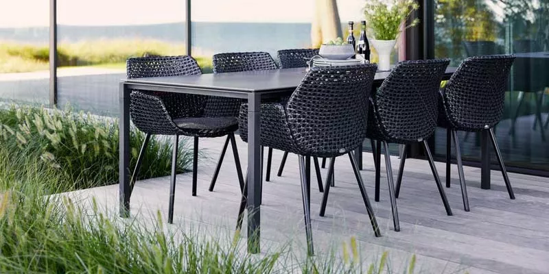 Cane-line Vibe Gartenmöbel-Set in Schwarz auf einer Terrasse mit Blick auf das Meer, bestehend aus einem Tisch und sechs Stühlen.