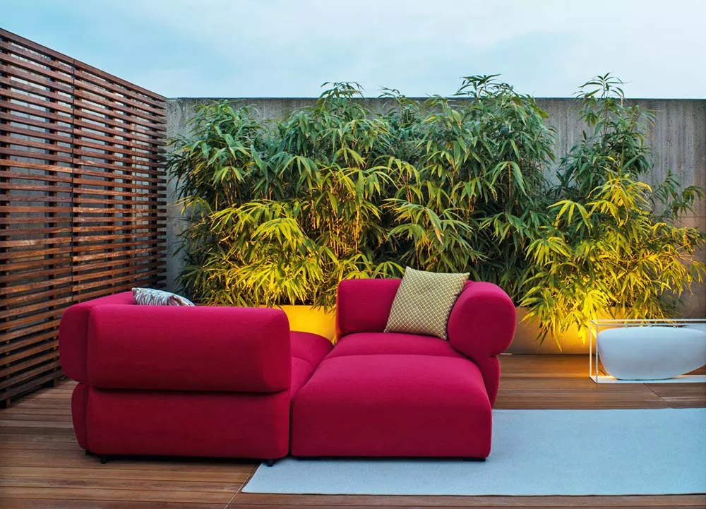 B&B Italia Butterfly Gartenmöbel Loungegruppe in Rot auf einer Terrasse mit Bambuspflanzen im Hintergrund und einem weißen Blumentopf.