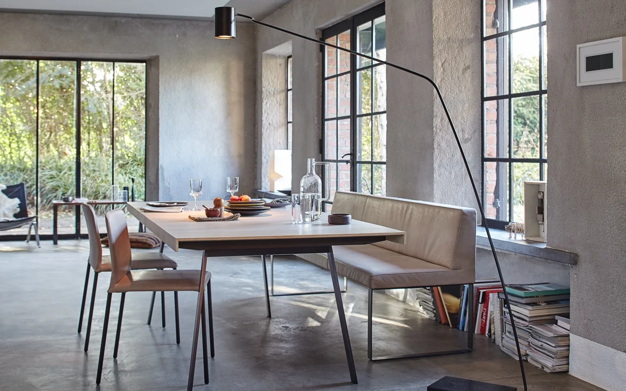 Braune BOP-Bank von more in modernem Esszimmer mit Betonwänden und großen Fenstern, stimmungsvolle Atmosphäre.