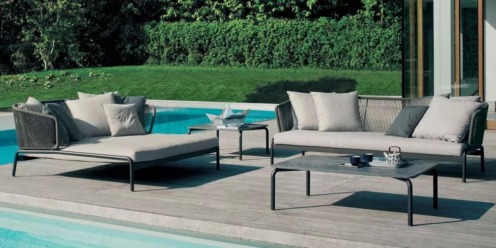 Roda Spool Loungegruppe in Grau auf einer Terrasse am Pool mit grüner Hecke im Hintergrund, bestehend aus Sofa, Liege und Tisch.