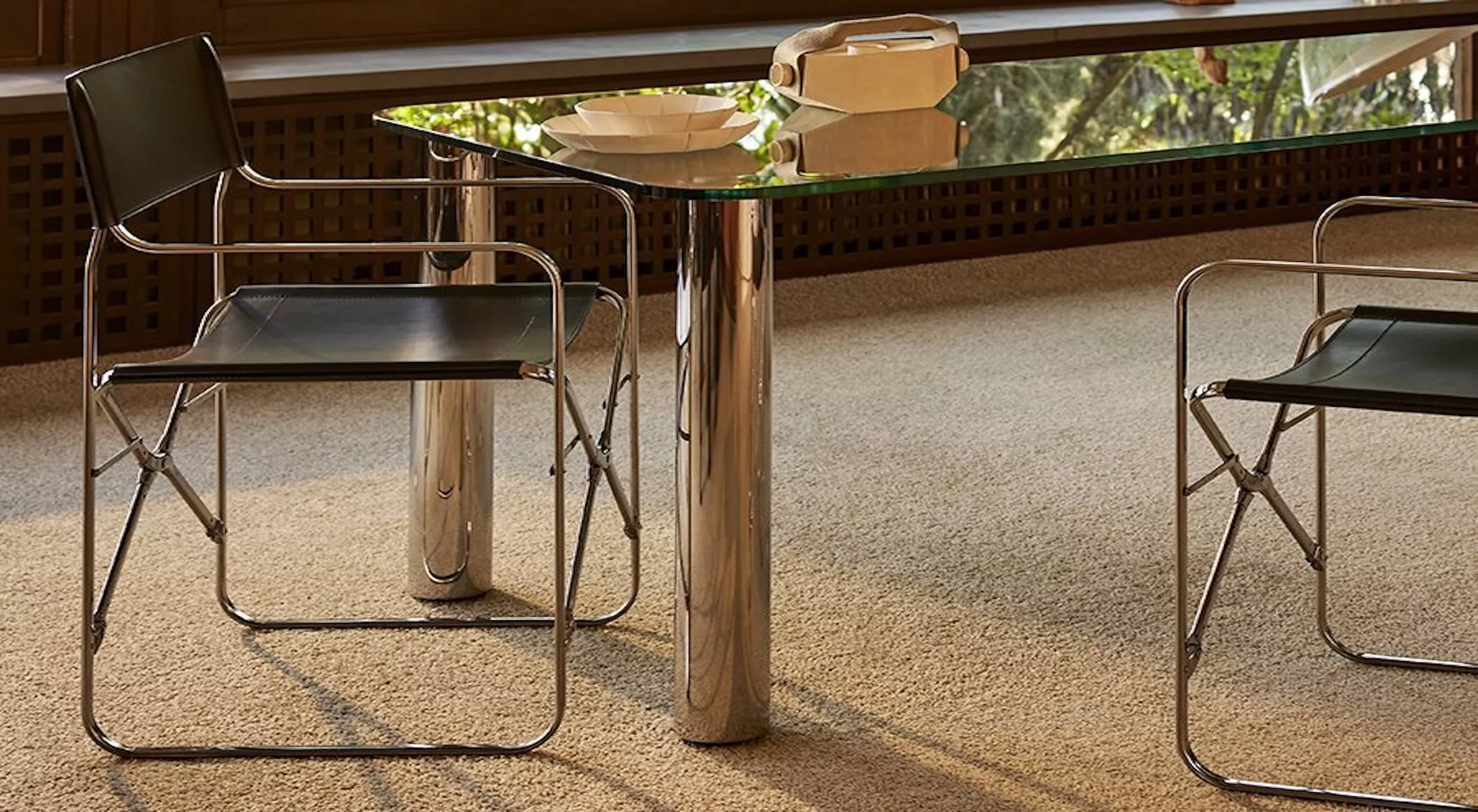 Ein eleganter Raum mit einem modernen Glastisch und zwei schwarzen Lederstühlen auf einem beigen Teppichboden, umgeben von Holzvertäfelung.