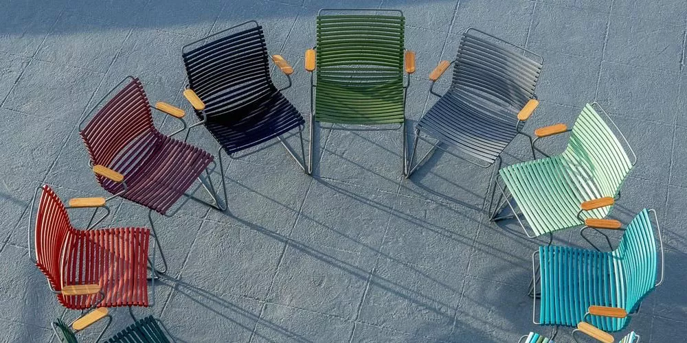 Houe Click Stühle in verschiedenen Farben, kreisförmig auf grauem Boden angeordnet, mit Holzarmlehnen, aus der Kollektion Click.