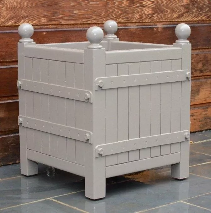 Orangerie Pflanzkübel aus lackiertem Akazienholz in quadratischer Form auf einem Steinboden vor einer Holzwand ohne Hintergrund