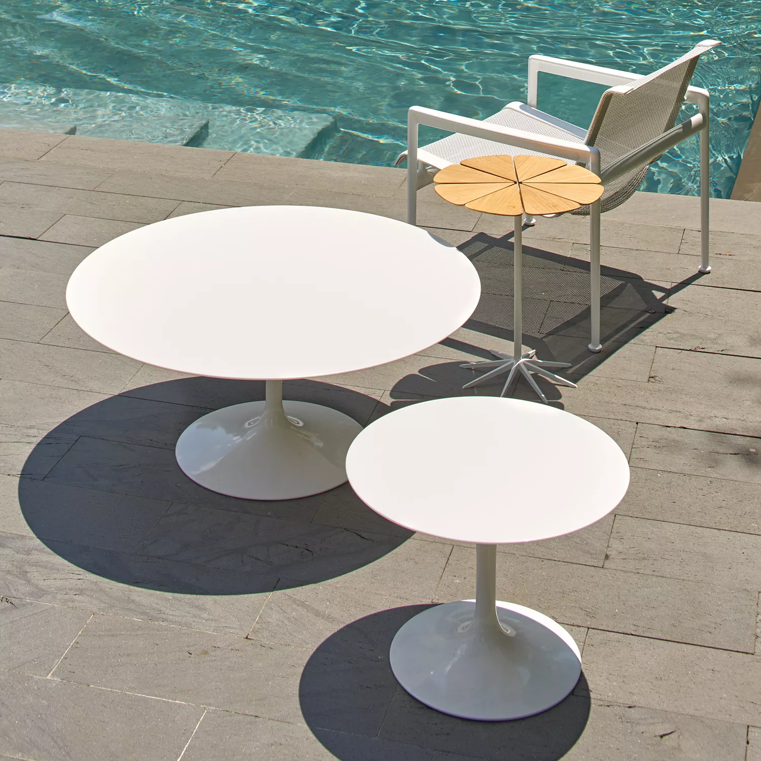 Knoll Saarinen runder Esstisch 107cm und kleiner Tisch auf einer Terrasse neben einem Pool mit einem weißen Stuhl im Hintergrund