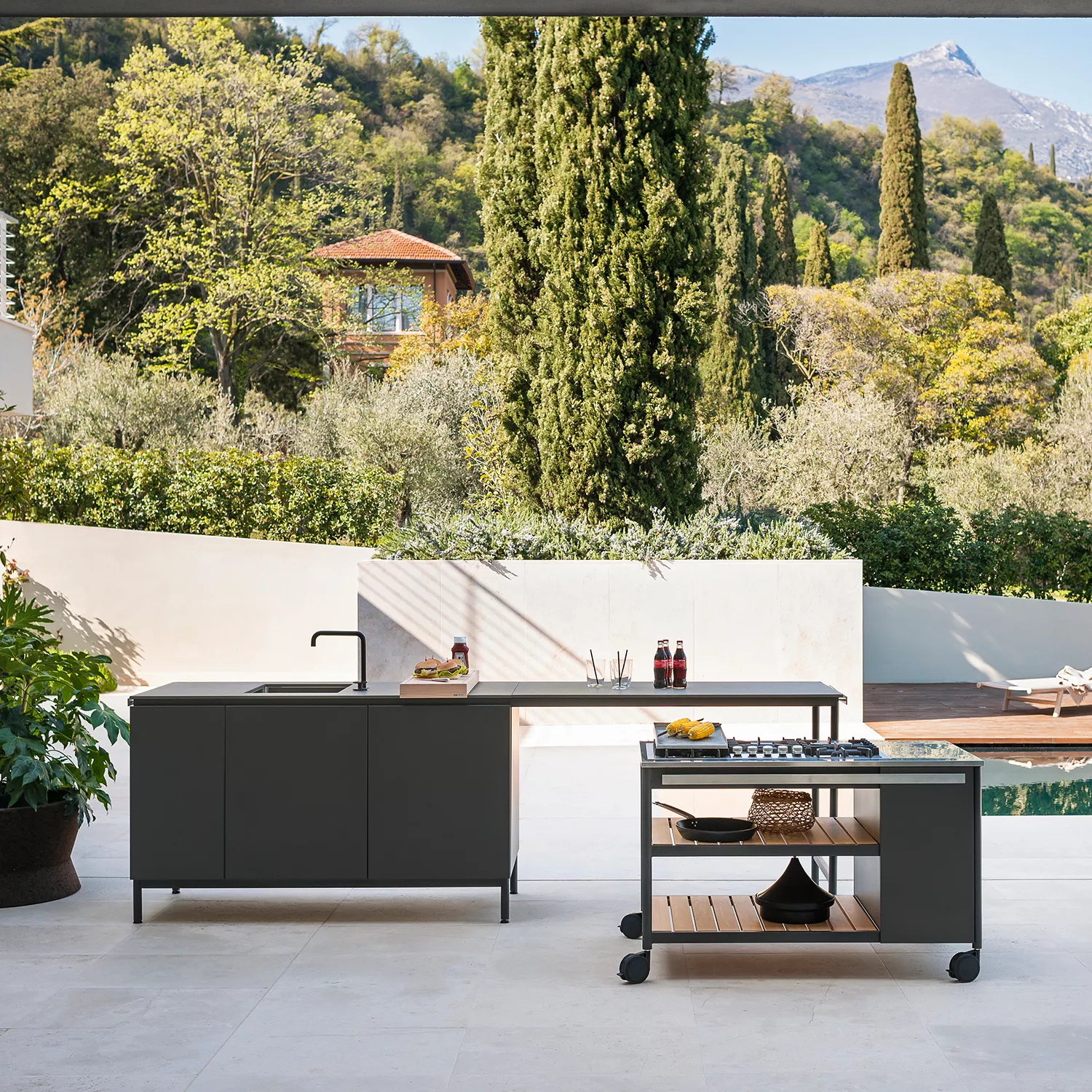 Roda Norma Küchenmodul in Anthrazit auf einer Terrasse mit Blick auf einen mediterranen Garten und Berge im Hintergrund.