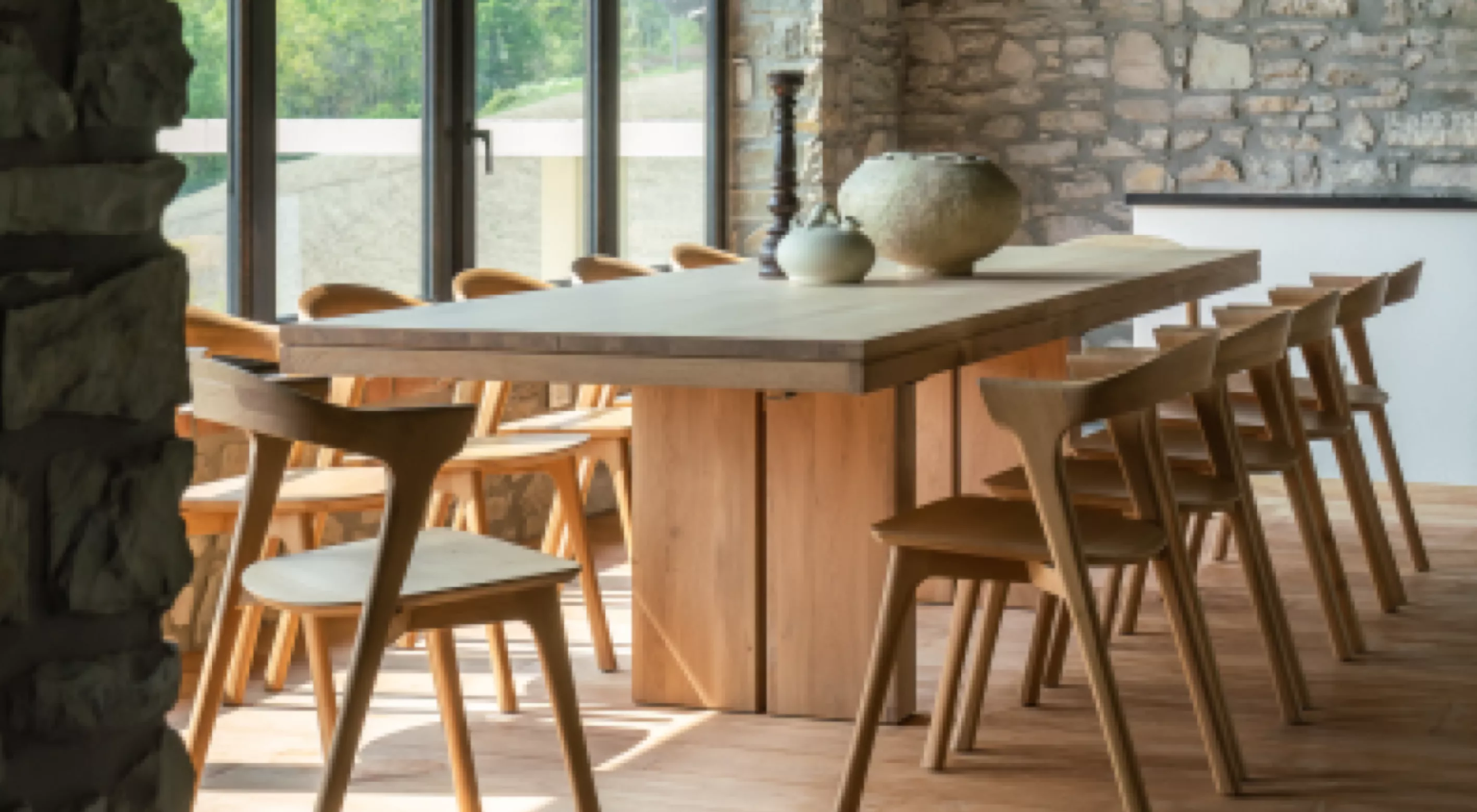Holztisch und Stühle von Villa Schmidt in einem modernen Esszimmer mit Steinwänden und großen Fenstern, die viel Licht hereinlassen.