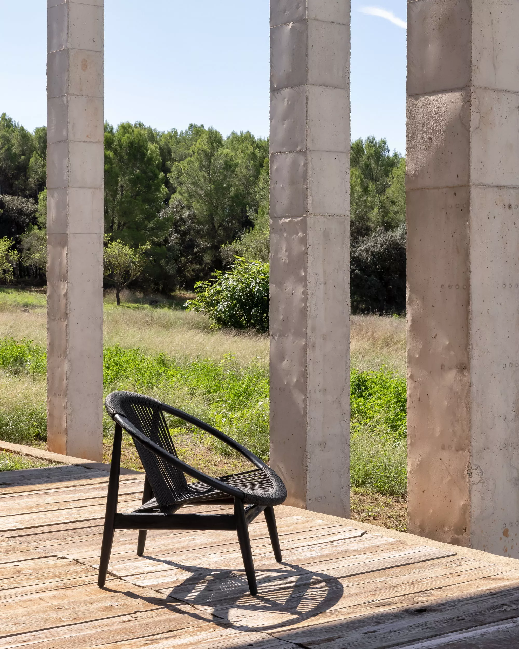 Vincent Sheppard Frida Lounge Chair in Schwarz auf einer Holzterrasse mit Blick auf eine grüne Landschaft und steinerne Säulen.
