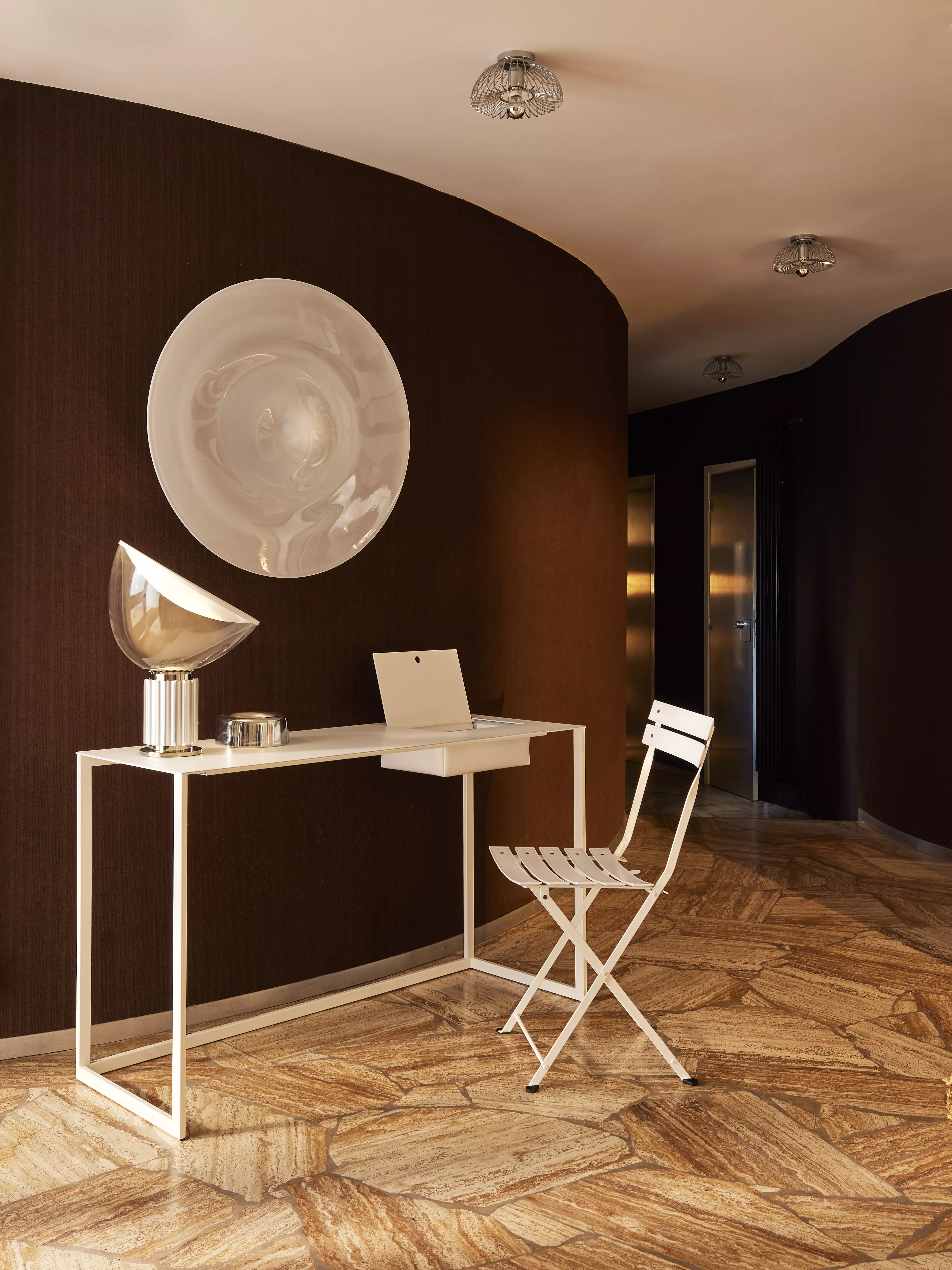 Zanotta Calamo Schreibtisch in einem modernen Raum mit brauner Wand und Kunstobjekten ein Laptop und eine Lampe stehen auf dem Schreibtisch