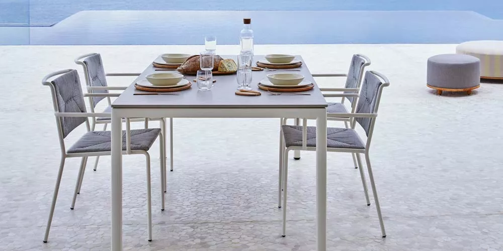 Outdoor-Essgruppe von Point in Weiß mit vier Stühlen und gedecktem Tisch vor einem Pool auf einer Terrasse.