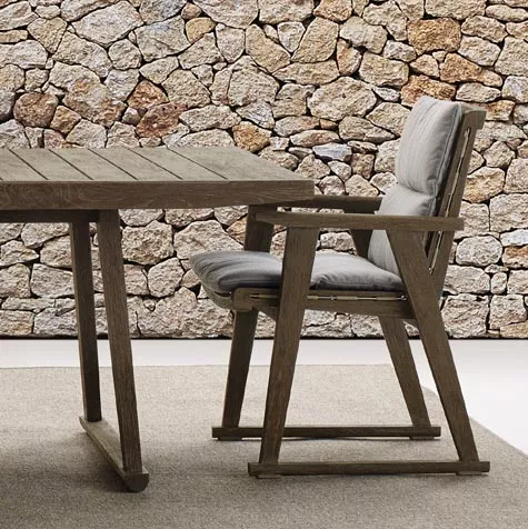 B&B Italia Gio Gartentisch 220 cm und Stuhl auf einem Teppich vor einer Steinmauer