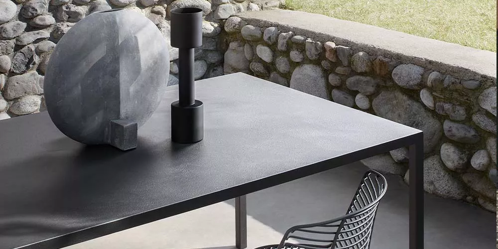 MDF Italia Tense Tisch in Schwarz auf einer Terrasse mit Steinmauer im Hintergrund, moderne und minimalistische Outdoor-Atmosphäre.