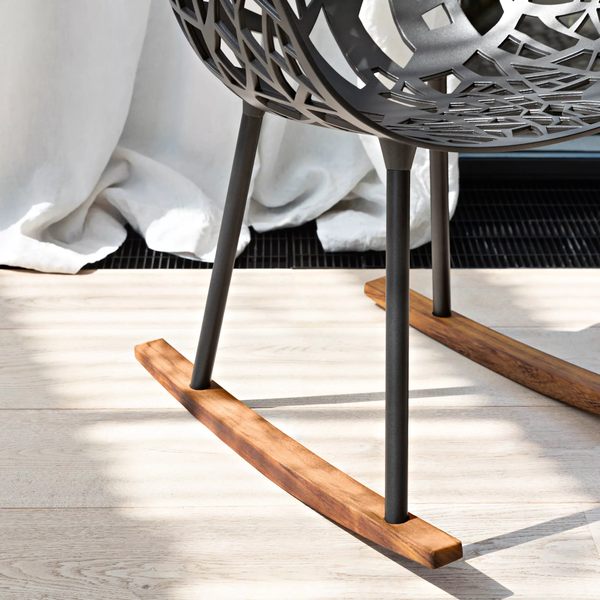 Fast Forest Schaukelstuhl in Anthrazit mit Holzbeinen, Detailansicht auf hellem Holzboden vor einem weißen Vorhang.