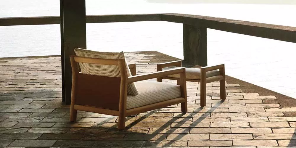 Zwei Beb Pablo Outdoor-Sessel in Holzoptik auf einer Terrasse mit Seeblick bei Sonnenuntergang.