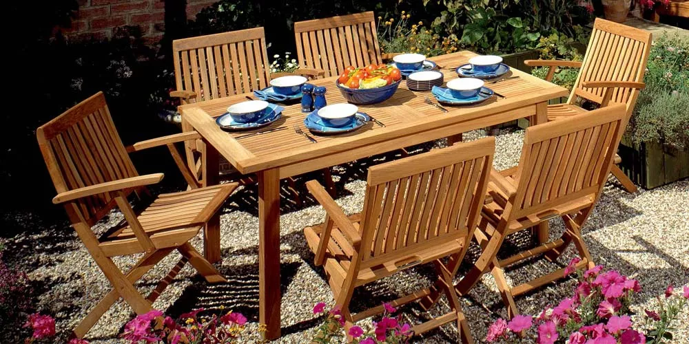 Barlow Tyrie Monaco Essgruppe aus Teakholz auf Kiesuntergrund, bestehend aus einem rechteckigen Tisch und sechs Stühlen, gedeckt für ein Essen im Freien.