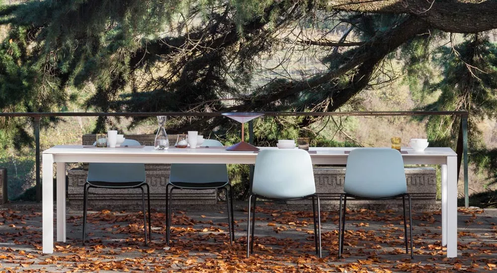 Lapalma APTA Outdoor Essgruppe in Weiß auf einer Terrasse mit Herbstlaub und Bäumen im Hintergrund, stimmungsvolles Ambiente.