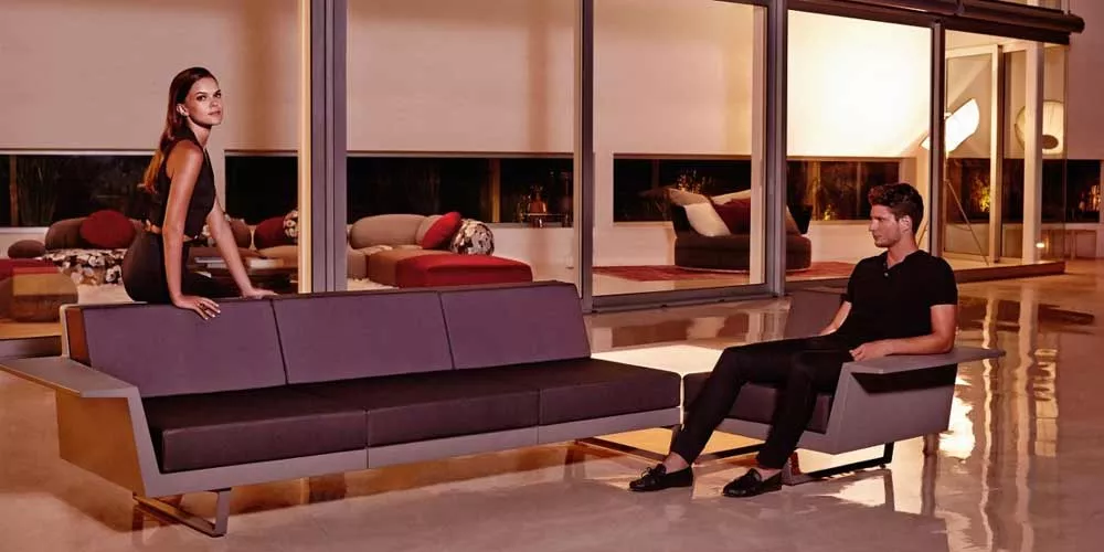 Vondom Delta Loungegruppe in Dunkelgrau, moderne Gartenmöbel auf poliertem Boden vor einem verglasten Hintergrund bei Abendstimmung.