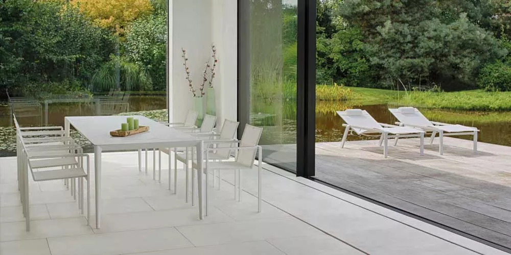 Royal Botania Red Label Alura Gartenmöbel in Weiß auf einer Terrasse mit Blick auf einen Teich und grüne Landschaft im Hintergrund.