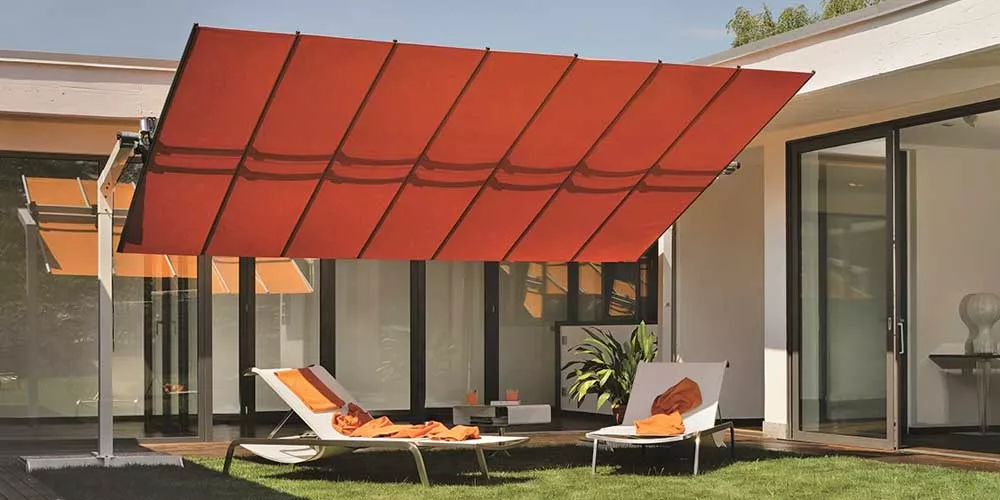 FIM Flexy Sonnenschirm in Orange über zwei Liegestühlen im modernen Garten, umgeben von weißen Wänden und Glasfenstern.
