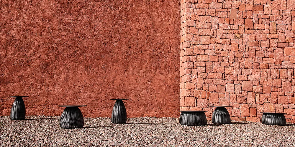 Dedon Kollektion Porcini Tische in Schwarz auf einem Kiesboden vor einer roten Steinmauer in einer Außenaufnahme.
