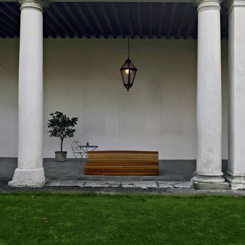 B&B Italia Titikaka Gartenbank steht unter einer überdachten Veranda neben einem kleinen Baum und einer Laterne im Hintergrund