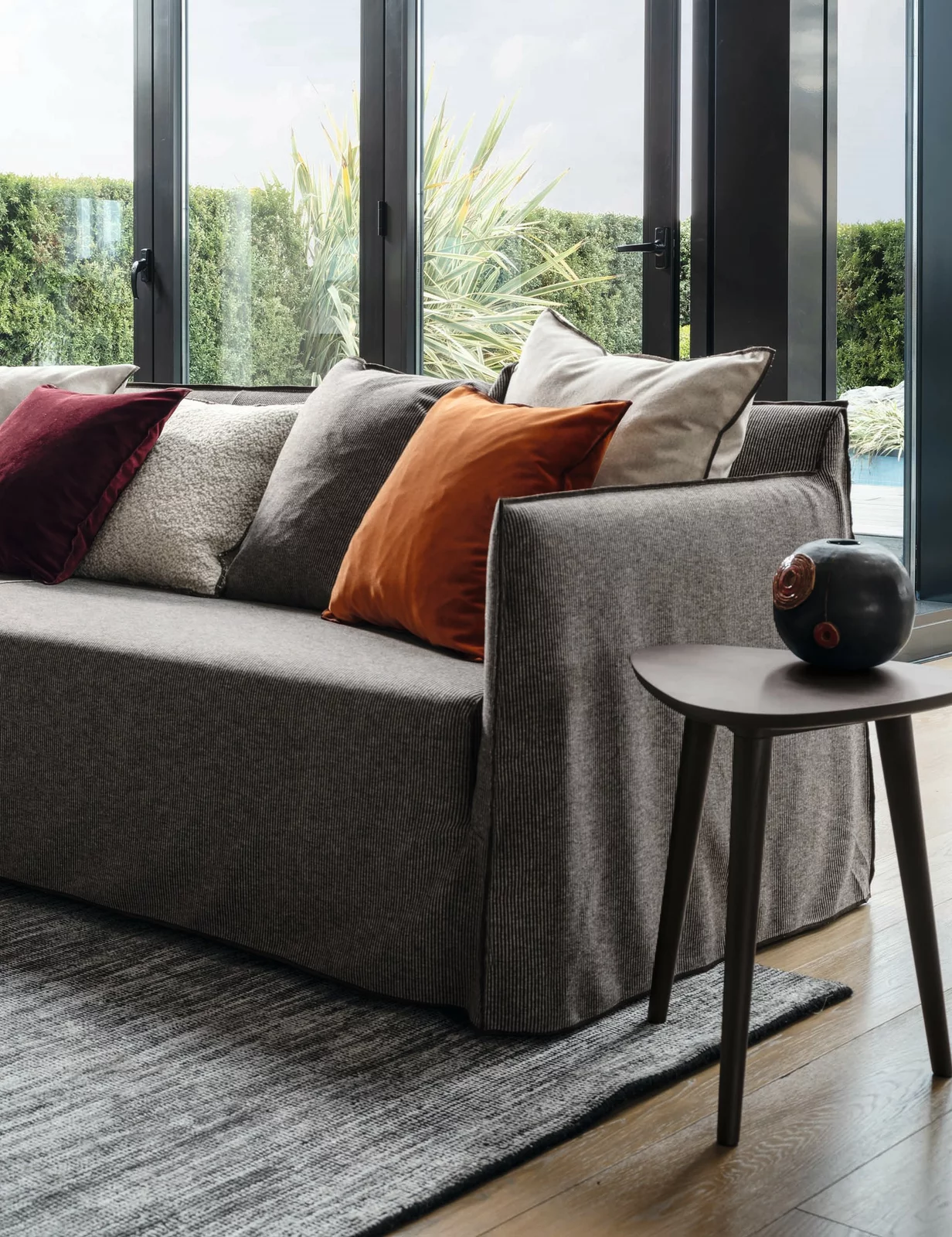 Gervasoni Sofa in einem modernen Wohnzimmer mit bunten Kissen und einem Beistelltisch vor großen Fenstern mit Blick auf den Garten