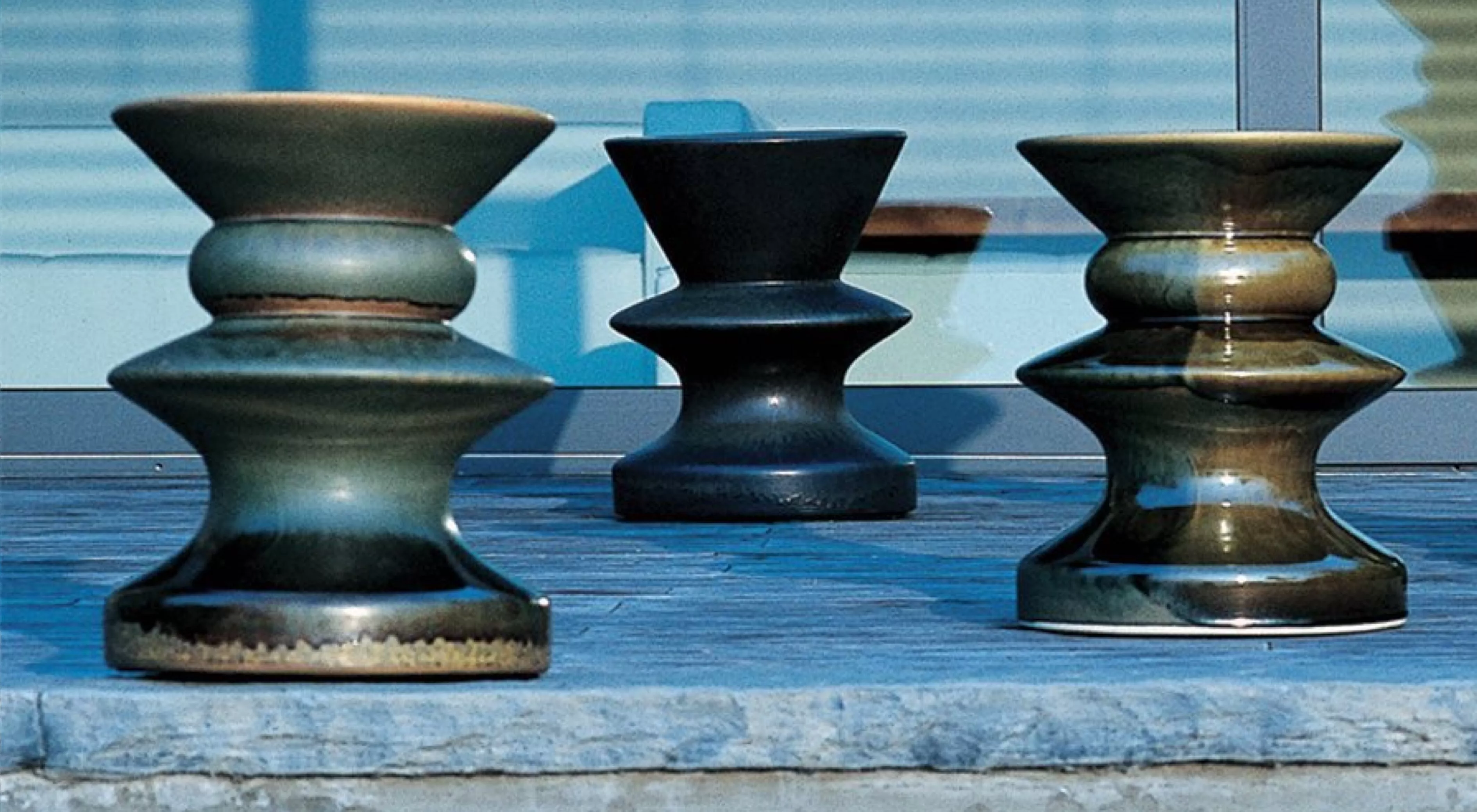 Drei Teti Hocker von Villa Schmidt in verschiedenen Grüntönen auf einer Steinplatte vor einer Glasfassade bei Tageslicht.