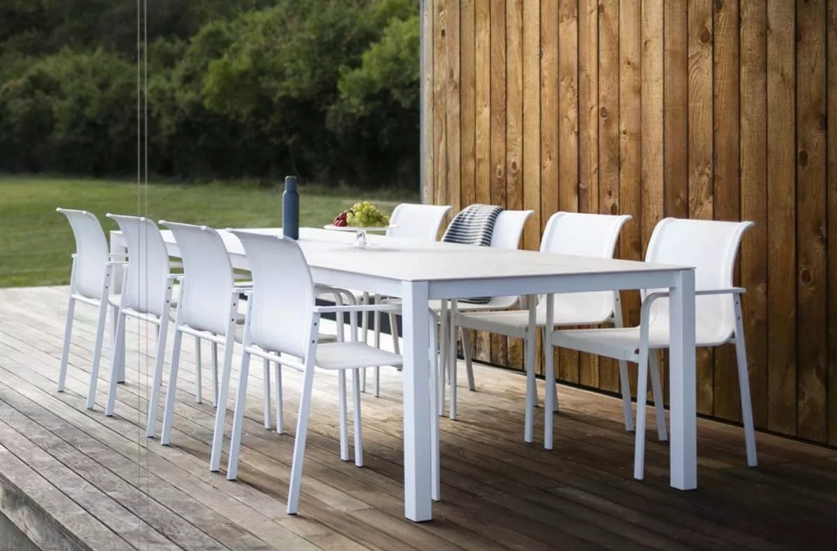 Todus Essgruppe in Weiß auf einer Holzterrasse vor einer Holzwand, bestehend aus einem Tisch und acht Stühlen, im Gartenambiente.
