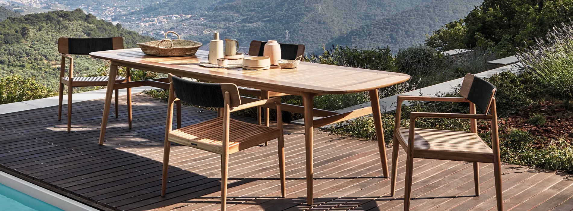 Canline Archi Stuhl in natürlichem Holzton auf einer Terrasse mit Bergblick, umgeben von einem Holztisch und weiteren Stühlen.