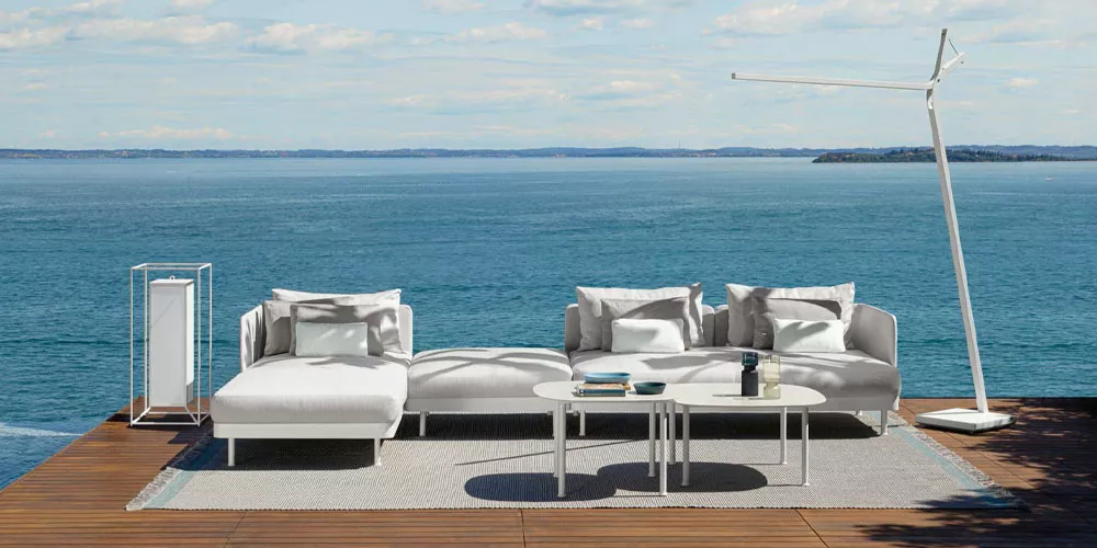 Talenti Kollektion Slam in Weiß auf einer Terrasse mit Meerblick, bestehend aus einem Sofa, einem Tisch und einer Stehlampe.