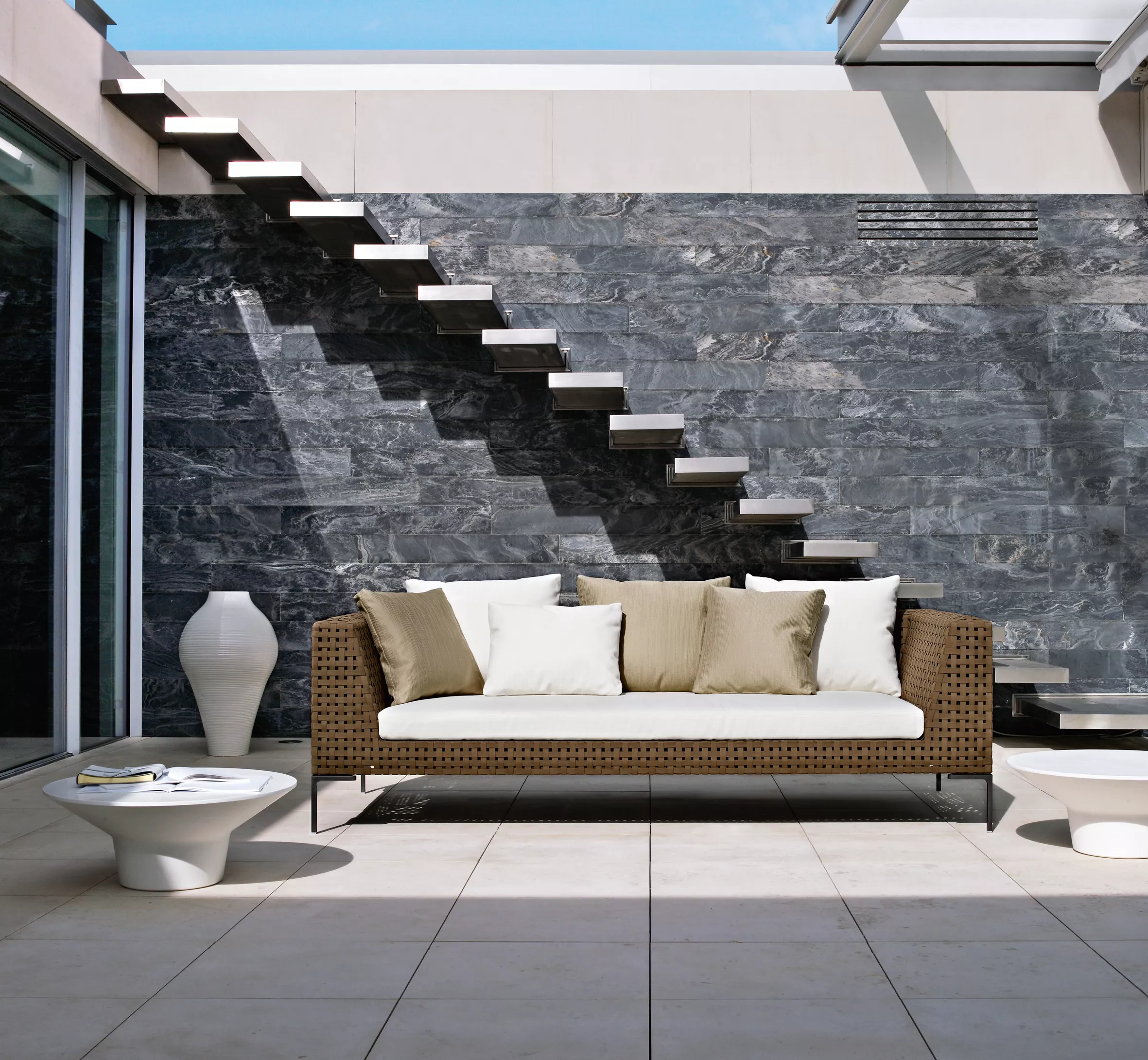 Charles Outdoor Sofa von B&B Italia auf einer modernen Terrasse mit Steinwand und Treppe im Hintergrund