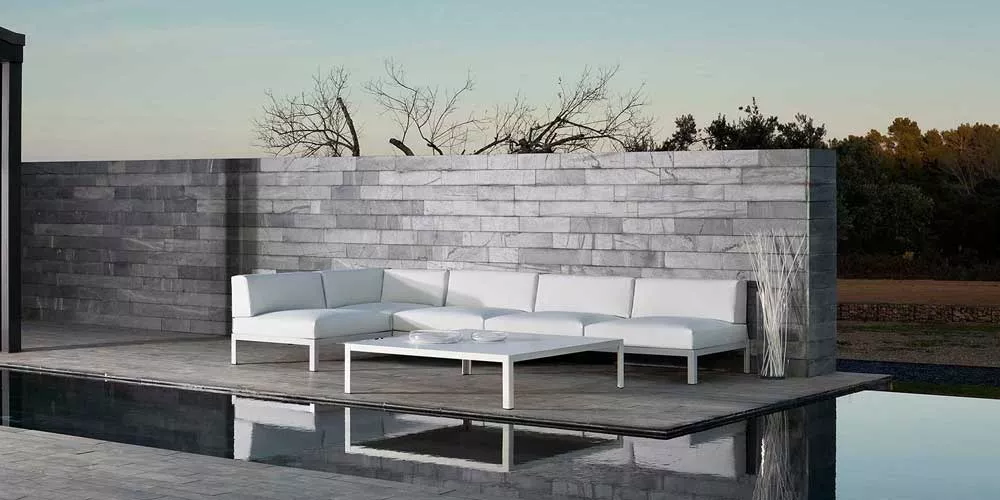 Bivaq NAK Loungegruppe in Weiß auf einer modernen Terrasse mit Steinwand und Pool im Hintergrund, stimmungsvolle Abenddämmerung.